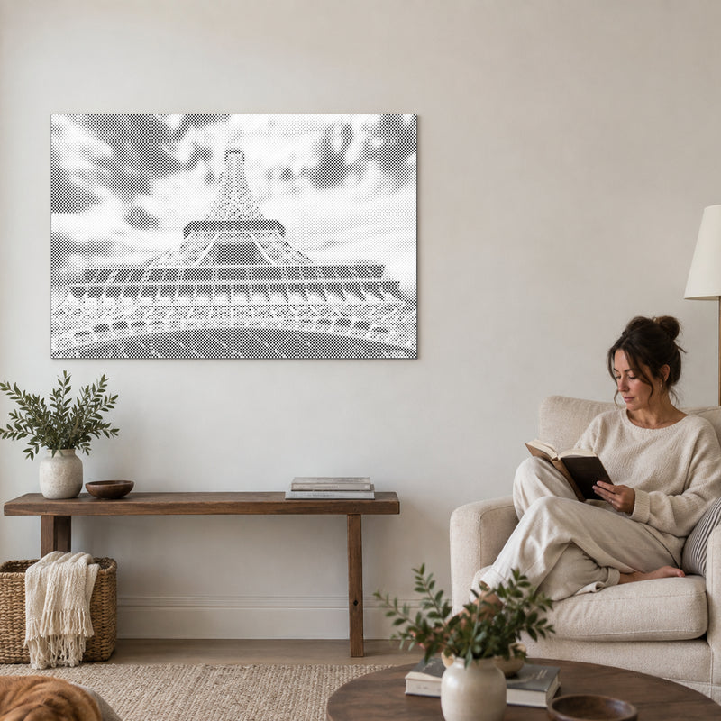 Dot-painting canvas “Eiffel Tower”, on a living-room wall with a person reading in an armchair nearby.