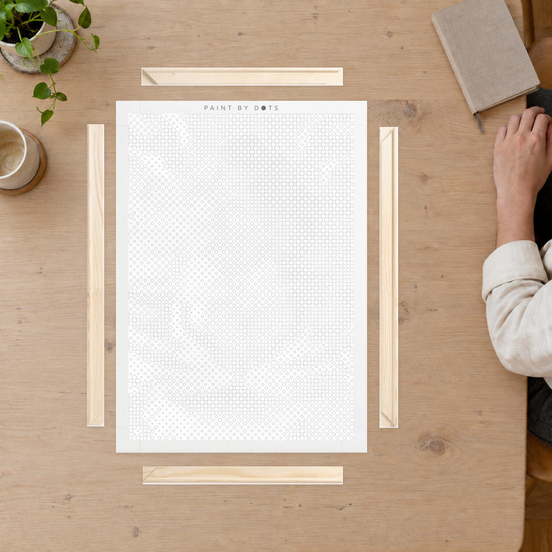 Wooden Frame Kit for Canvas, on a craft table with a person’s hand resting at the edge.